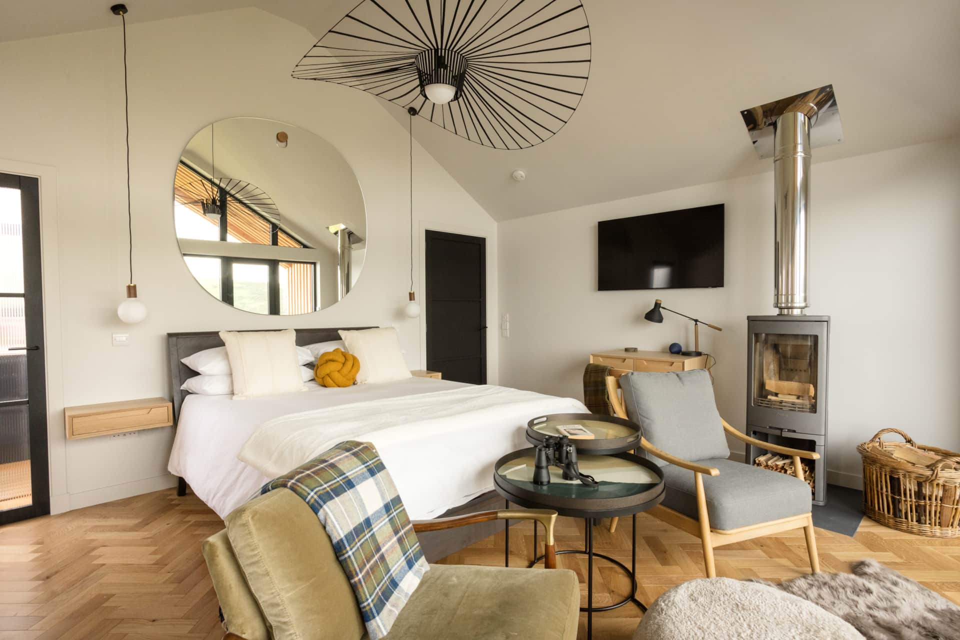 Bedroom with round mirror, wall-mounted TV, and log burner