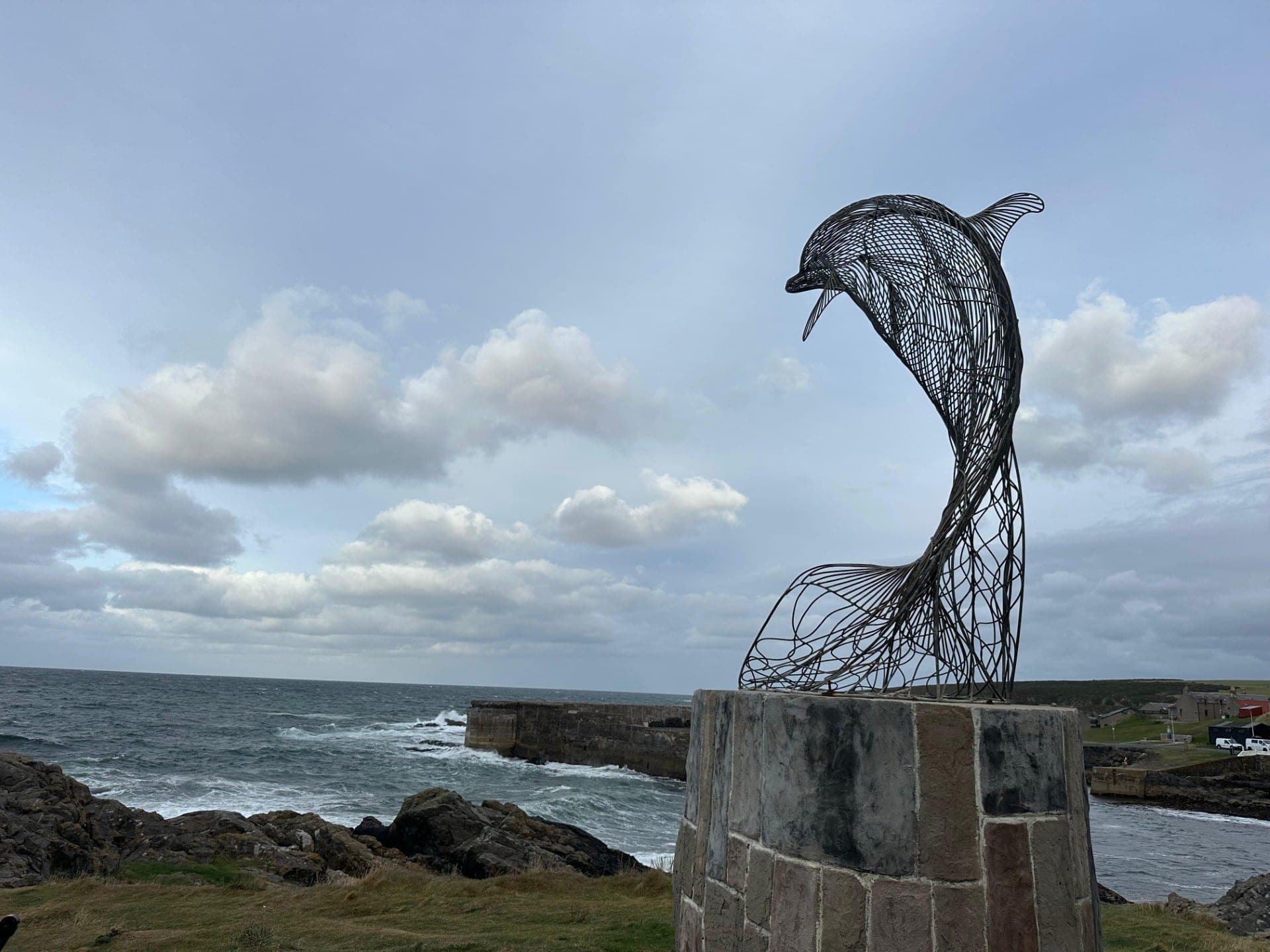 The Portsoy Dolphin, a wire sculpture on a stone plinth overlooking the sea at Portsoy