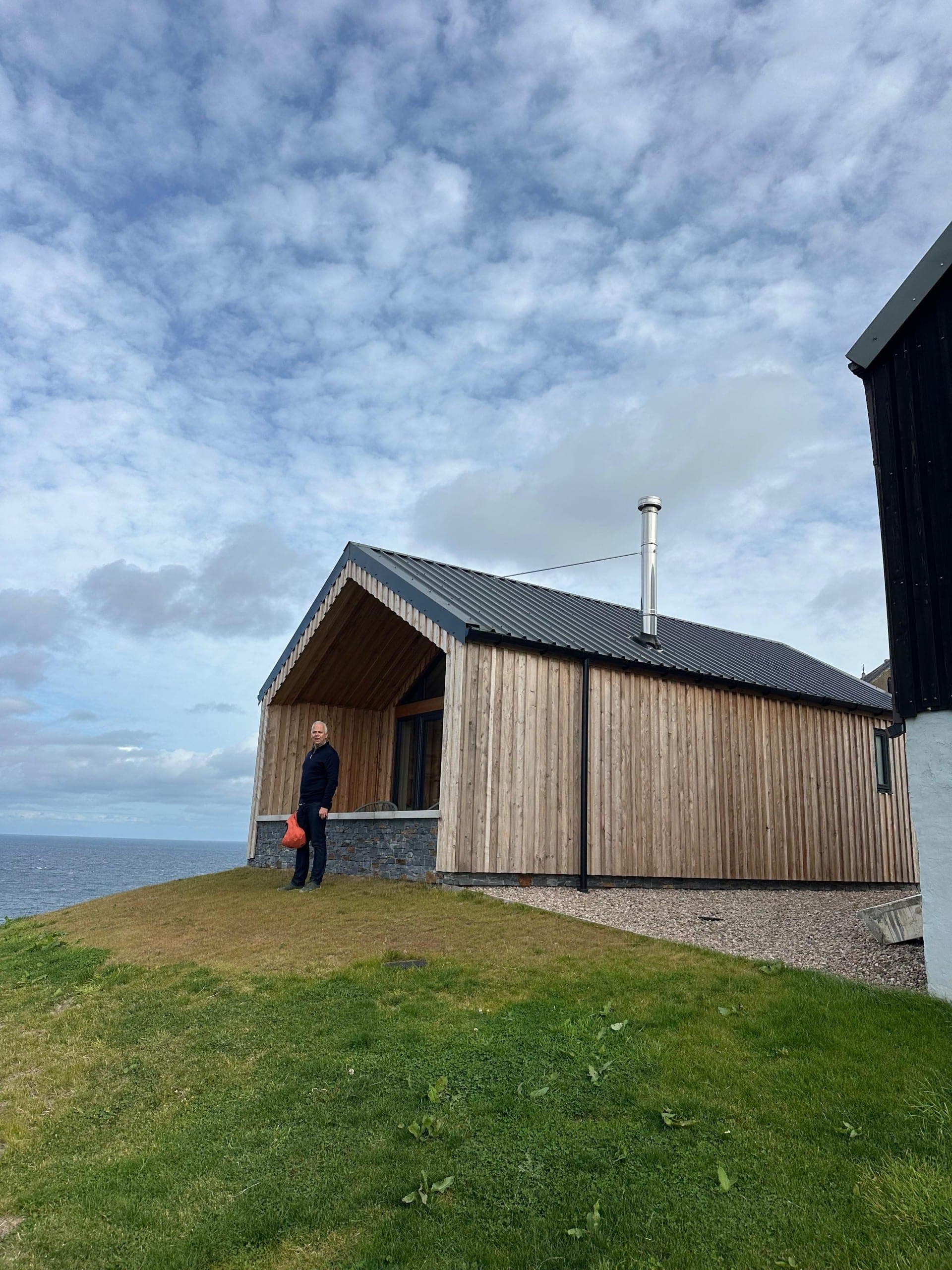 Our guest outside the timber-clad Muckle View chalet on the clifftop, with the sea behind