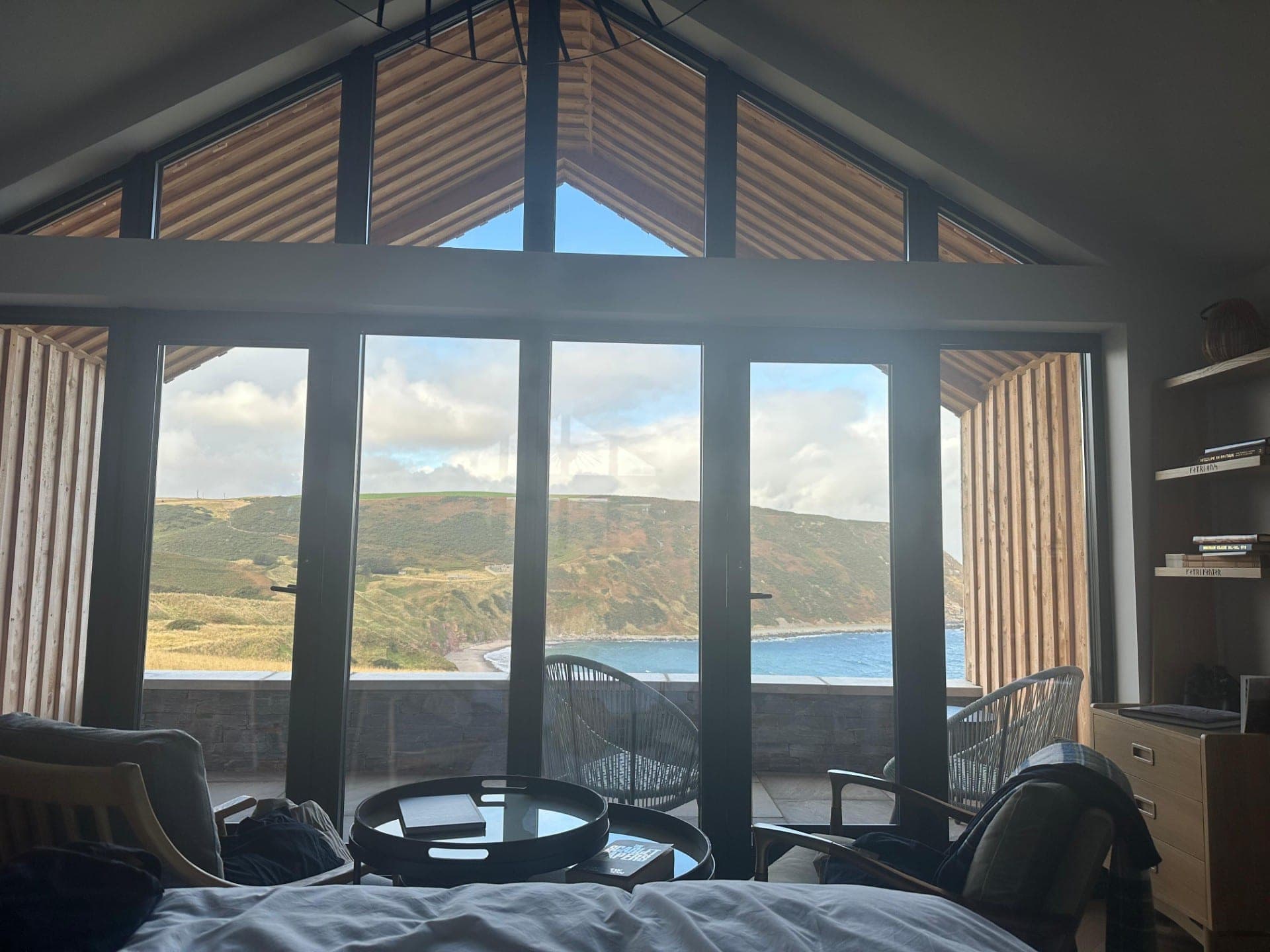 The view from the bed through Muckle View's full-width A-frame window to the balcony, the bay and the green headland